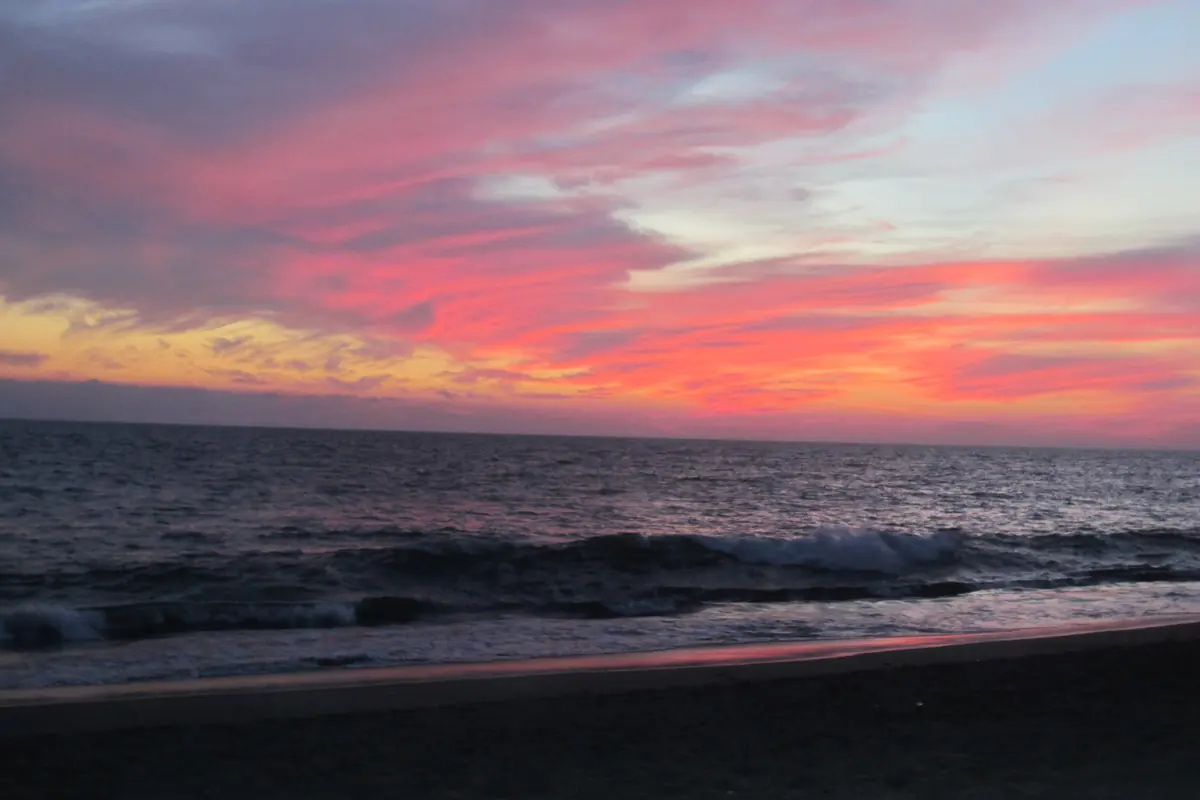 A pink and orange sunset sky above dark waves and a dark beach (a sunset over Banderas Bay seen from the shore in Puerto Vallarta, not from the boat)